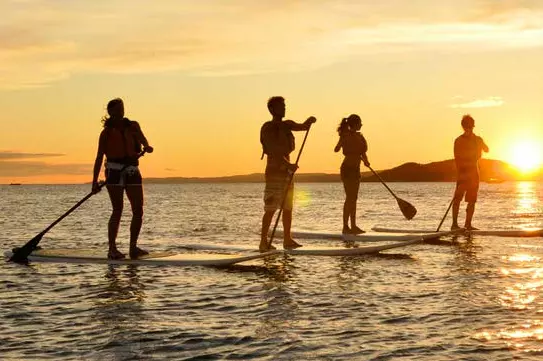 Quatre personnes debout et pagayant à bord au coucher du soleil