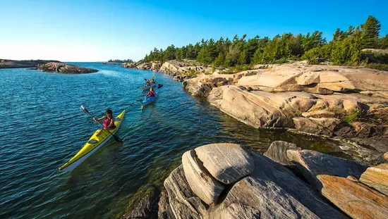 Trois personnes qui pagaient le long d’un lac près d’un terrain rocheux contenant des arbres.